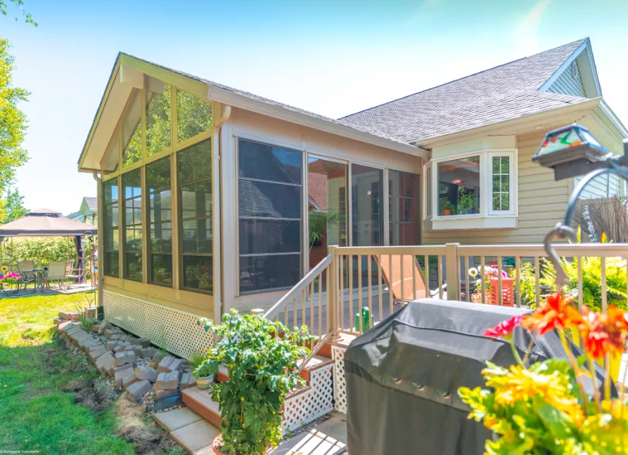 Custom sunroom with large windows, wooden deck, and surrounding greenery in a residential backyard, enhancing outdoor living space in Scarborough, Maine.
