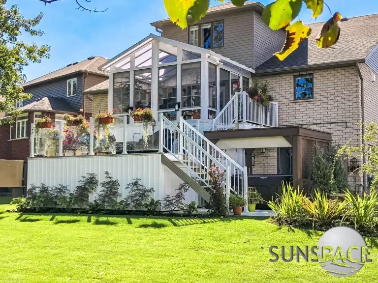 Sunspace Sunroom with glass railing and outdoor patio, featuring lush greenery and decorative flowers, enhancing outdoor living spaces in Scarborough, ME.