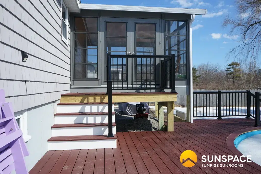 Custom sunroom with glass windows and door, surrounded by wooden steps and deck, showcasing Sunspace branding, designed for outdoor living enhancement in Portland, ME.