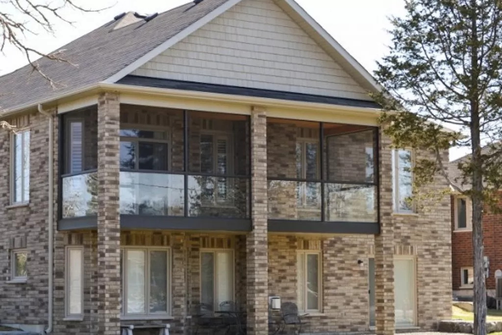 Newly constructed sunroom with glass railing and brick exterior, enhancing outdoor living space in residential setting.