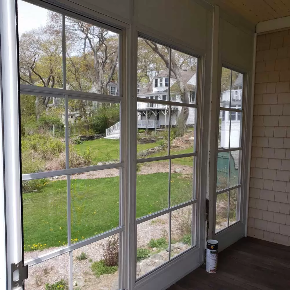 Interior view of a sunroom with large windows showcasing a landscaped yard and nearby houses, emphasizing outdoor connectivity and natural light.