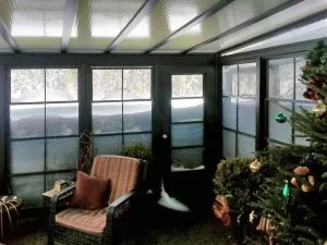Cozy sunroom interior with large windows showing snow accumulation outside, featuring a comfortable chair and festive decorations, illustrating winter living solutions for Maine homes.