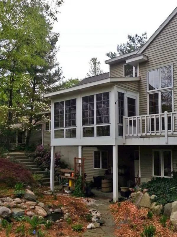 Porch enclosure featuring WeatherMaster windows, seamlessly integrated into a home’s architecture, surrounded by a landscaped garden, enhancing outdoor living space.